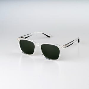 May include: Clear frame sunglasses with dark green lenses. The sunglasses have a classic rectangular shape.