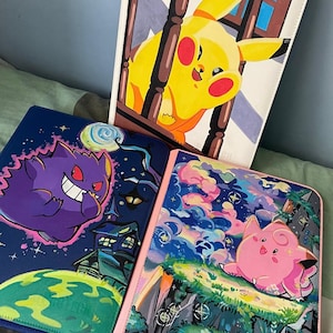 Op de afbeelding: Drie rechthoekige mappen met kleurrijke illustraties. Eén map toont een geel personage achter houten leuningen. Een andere toont een paars personage boven een groene planeet en een donker huis. De derde toont een roze personage op een klif.