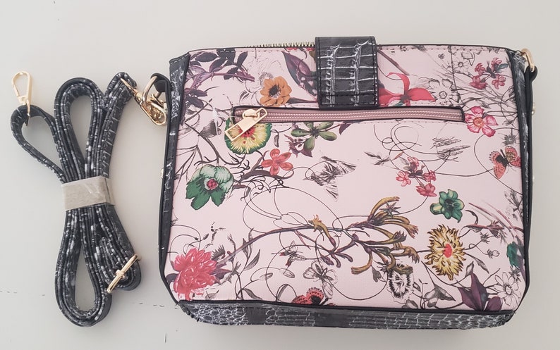 May include: A pink floral crossbody bag with a black and white patterned strap. The bag has a flap closure with a gold buckle and a zippered pocket on the front.