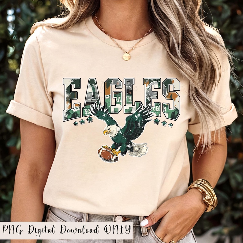 May include: A beige t-shirt featuring the word "EAGLES" in a green camouflage design. Below the word is a graphic of an eagle holding a football. The text "PNG Digital Download ONLY" is at the bottom.