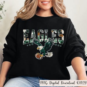May include: Black sweatshirt with the word "EAGLES" in a green and white camouflage pattern. Below the word is a graphic of an eagle holding a football. The text "PNG Digital Download ONLY" is at the bottom.