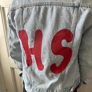 May include: A light blue denim jacket with the letters "HS" in red outlined with rhinestones on the back.