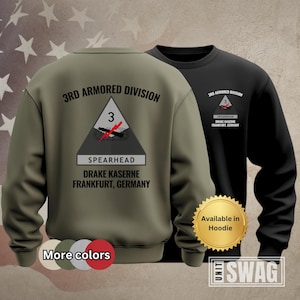 May include: Two sweatshirts, one olive green and one black, featuring the text "3RD ARMORED DIVISION" and a triangular emblem with a tank graphic. The text "SPEARHEAD DRAKE KASERNE FRANKFURT, GERMANY" is below the emblem. The olive green sweatshirt has "More colors" text.