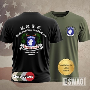May include: Two t-shirts, one black and one olive green, with military-themed graphics. The black shirt features text and a crest that reads "Jungle Operations Training Center" and "Jungle Expert." The olive shirt has a similar design. The shirts are available in long sleeve.