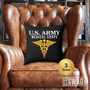 May include: A black throw pillow with white text that reads "U.S. ARMY MEDICAL CORPS" and a gold medical caduceus symbol. The pillow is on a brown leather armchair.
