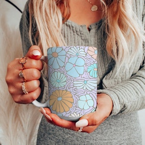 May include: A white ceramic mug with a colorful floral pattern. The pattern features blue, pink, and yellow flowers on a light purple background.