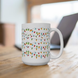 May include: White ceramic mug featuring a colorful string of Christmas lights design. The lights are in various colors, including red, green, blue, and yellow. The mug has a large handle and is suitable for hot beverages.