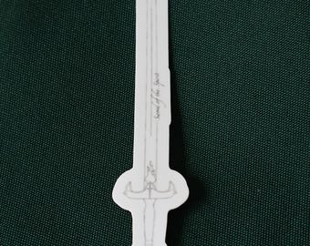 May include: A white sticker with a black outline of a sword. The sword has a cross guard and a circular pommel. The text "Sword of the Spirit" is written on the blade.