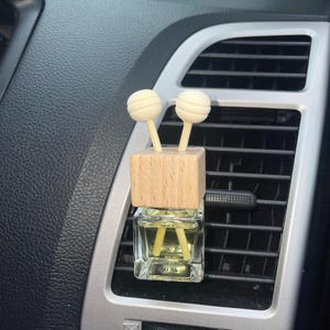 May include: A wooden car air freshener with two white diffuser sticks and a clear glass bottle filled with yellow liquid.