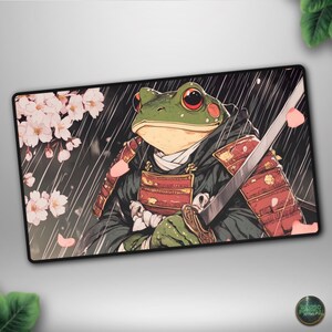 May include: A rectangular mousepad featuring a cartoon illustration of a frog dressed as a samurai, holding a katana. The frog is green with red eyes and is wearing a black and red samurai outfit. Cherry blossoms and rain are in the background.