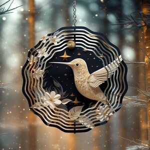 May include: A gold and white metal wind chime featuring a hummingbird with a black and gold background. The wind chime has a circular shape and is decorated with flowers and stars.