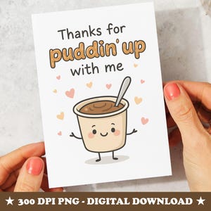 May include: A white card with the text "Thanks for puddin' up with me" and a cartoon image of a pudding cup with a spoon. The pudding cup has a smiling face and arms. Small pink and peach hearts are scattered around the image.