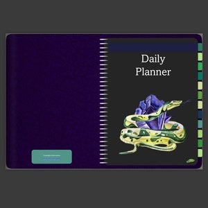 May include: A purple daily planner with a black cover featuring a green snake coiled around a purple crystal. The text "Daily Planner" is printed in white on the cover.