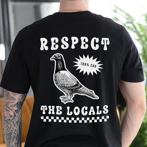 Peut inclure: T-shirt noir avec un imprimé graphique blanc d'un pigeon et le texte "RESPECT 100% COO THE LOCALS"