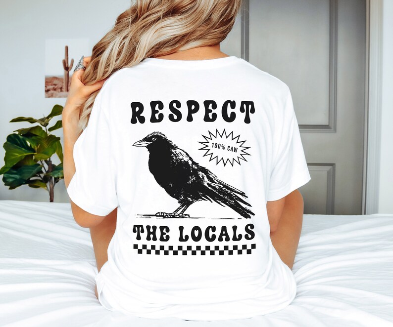 May include: White t-shirt with a black graphic of a crow and the text "RESPECT THE LOCALS." The crow is standing on a line, with the words above and below it. A starburst graphic reads "100% CAW."