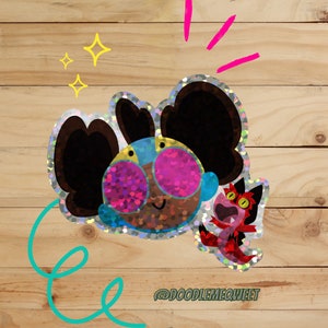 May include: A holographic sticker featuring a cartoon character with large, black hair, blue and yellow eyes, and pink sunglasses. A smaller, red holographic sticker of a cartoon creature with a wide mouth and yellow eyes is also included. The stickers are on a wooden background with the text "@doodlemequeet".