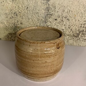 May include: A round, beige ceramic jar with a lid. The jar has a speckled glaze and a slightly textured surface.