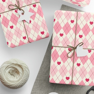 May include: Two pink and white gift boxes wrapped in a pink and white argyle pattern with pink hearts. The boxes are tied with brown twine and have white paper tags attached.