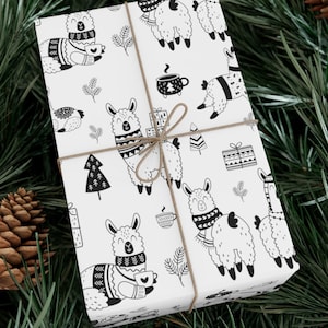 May include: White gift wrap featuring a repeating pattern of black and white llamas wearing sweaters and scarves, holding mugs, and surrounded by Christmas trees and gifts. The wrapped gift is tied with twine and set on a bed of pine needles.