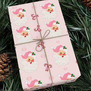 May include: Pink wrapping paper with a repeating pattern of Santa Claus faces and candy canes. The paper is tied with a brown ribbon.