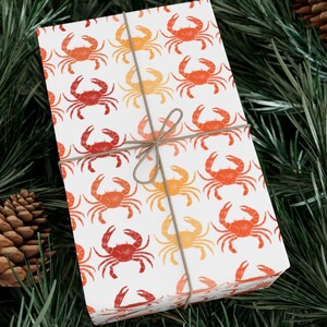 May include: White gift wrap with a repeating pattern of red and orange crabs. The wrapping paper is tied with a brown twine bow.