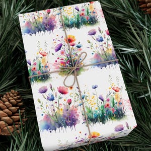 May include: White gift wrap with a watercolor pattern of colorful wildflowers and green grass. The paper is tied with a brown twine bow.
