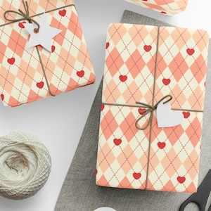 May include: Two gift boxes wrapped in pink and white patterned paper with red hearts. The boxes are tied with brown twine and have white paper tags attached.