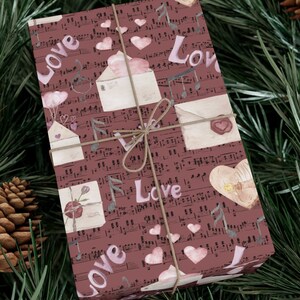 May include: A brown gift wrap with a musical note pattern and pink hearts. The words "Love" are repeated throughout the design. The gift wrap is tied with a brown twine bow.