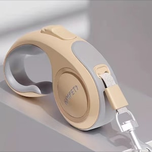 Op de afbeelding: Een beige intrekbare hondenriem met een grijze handgreep en een zilveren haak. De riem heeft het woord "HIMPET" aan de zijkant.