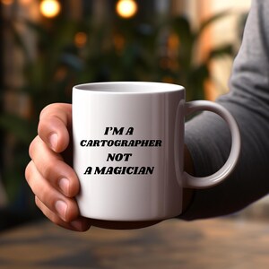May include: White ceramic mug with black text that reads "I'm a Cartographer Not a Magician".