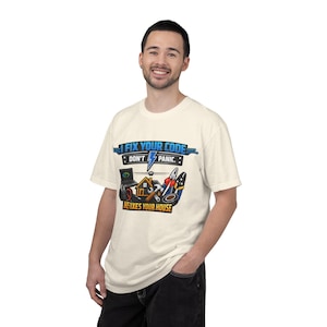 Może przedstawiać: Kremowy t-shirt z krótkim rękawem z nadrukiem graficznym zawierającym tekst I FIX YOUR CODE DON'T PANIC oraz HE FIXES YOUR HOUSE. Wzór zawiera ilustracje laptopa, domu, młotka oraz różnych narzędzi ręcznych.