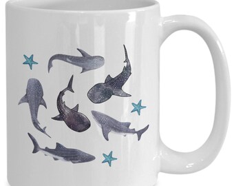 May include: White ceramic mug with a design of six whale sharks and five blue starfish. The whale sharks are swimming in a circle around the mug.