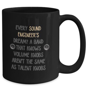 Könnte beinhalten: Schwarze Keramik-Tasse mit weißem Text: "EVERY SOUND ENGINEER'S DREAM? A BAND THAT KNOWS VOLUME KNOBS AREN'T THE SAME AS TALENT KNOBS." Mit zwei Lautsprecher-Symbolen. Ein Geschenk für Tontechniker.
