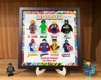 May include: A framed picture with a comic book theme featuring Lego minifigures of superheroes. The text reads "DADDY you are... as smart as IRON MAN, as strong as HULK, as mighty as THOR, as cool as BATMAN, as funny as SPIDERMAN, as kind as SUPERMAN, as tough as WOLVERINE, as brave as CAPTAIN AMERICA. You are our superhero! Love, Emma & Alex."