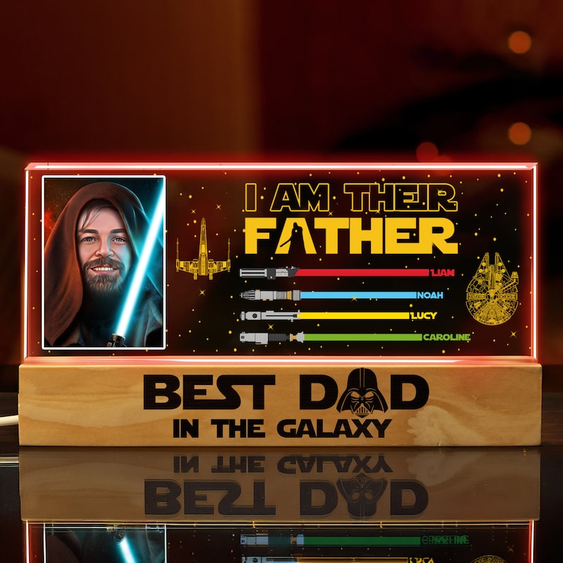 K&ouml;nnte beinhalten: Ein beleuchtetes Holzschild mit Star Wars-Motiv. Das Schild zeigt ein Bild von Obi-Wan Kenobi, ein Lichtschwert, einen Sternenzerst&ouml;rer und den Text "Ich bin ihr Vater." Unter dem Bild befindet sich eine Liste mit Namen: Liam, Noah, Lucy und Caroline. Am unteren Rand des Schildes steht "Bester Papa der Galaxie".