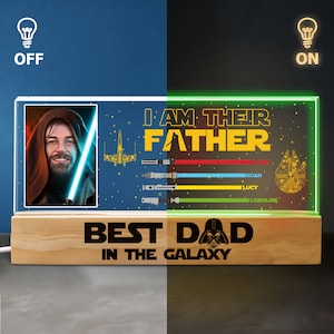 K&ouml;nnte beinhalten: Ein beleuchtetes Holzschild mit Star Wars-Motiv. Das Schild zeigt ein Bild eines Jedi-Ritters mit einem Lichtschwert, einem Raumschiff und dem Text "Ich bin ihr Vater". Unter dem Bild steht der Text "Bester Papa der Galaxie" mit einer Darth Vader-Grafik. Das Schild hat einen Lichtschalter an der Seite.