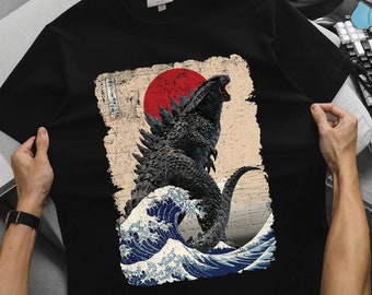 May include: Black t-shirt with a graphic print of a Godzilla-like monster standing on a wave with a red sun in the background.