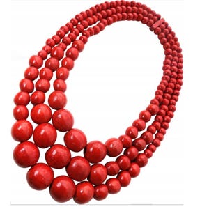 May include: A three-strand necklace featuring vibrant red beads. The necklace has varying bead sizes, with larger beads at the front and smaller ones towards the back. The beads are evenly spaced and strung together, creating a bold and eye-catching accessory.