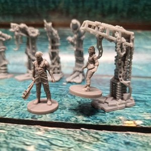 Könnte beinhalten: Ein Set aus vier grauen Plastik-Miniaturfiguren, darunter eine Figur mit einer Waffe, eine Figur mit einer Kette und zwei Figuren, die auf einer Basis stehen. Die Figuren stehen auf einer blauen Holzoberfläche.