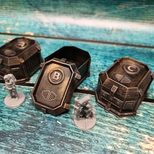 Puede incluir: Tres pequeños contenedores metálicos en forma de caja con un acabado desgastado, envejecido y desgastado. Cada caja tiene una letra, A, B y C, en la parte superior. Las cajas están sobre una superficie de madera azul y verde.