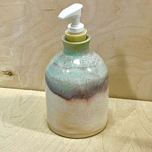 Pu&ograve; includere: Un dispenser di sapone in ceramica dal corpo arrotondato con smalto reattivo nelle tonalit&agrave; crema, verde tenue e viola spento. Il contenitore presenta un collo stretto ed &egrave; sormontato da una pompa in plastica bianca per il sapone liquido.
