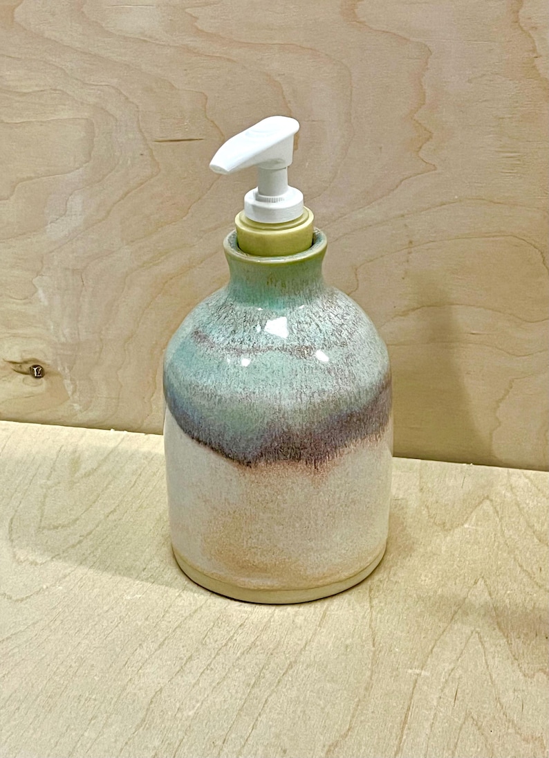 Pu&ograve; includere: Un dispenser di sapone in ceramica dal corpo arrotondato con smalto reattivo nelle tonalit&agrave; crema, verde tenue e viola spento. Il contenitore presenta un collo stretto ed &egrave; sormontato da una pompa in plastica bianca per il sapone liquido.