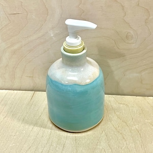 Pu&ograve; includere: Un dispenser per sapone in ceramica con corpo arrotondato, caratterizzato da una smaltatura turchese lucida nella parte inferiore e una smaltatura bianca liscia sul collo superiore. Il dispenser &egrave; dotato di una pompa in plastica bianca.