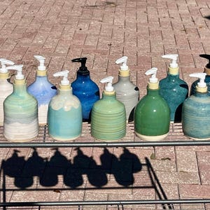 Pu&ograve; includere: Una collezione di dieci dispenser per sapone in ceramica con vari colori di smalto, tra cui bianco, azzurro, verde acqua, blu scuro e verde. Ogni flacone presenta una base arrotondata, un collo stretto e una pompa in plastica bianca o nera.