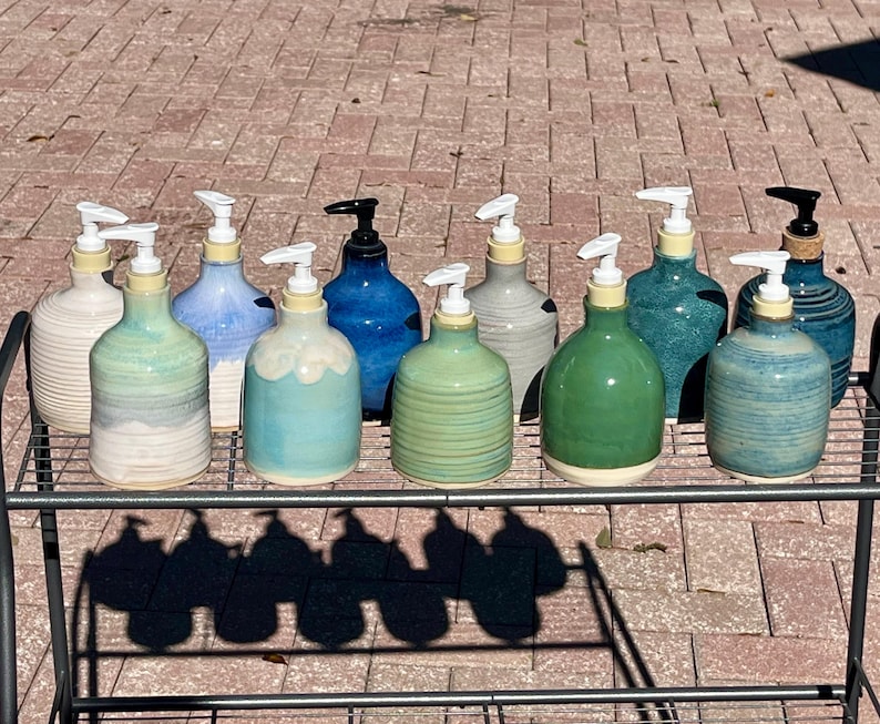 Pu&ograve; includere: Una collezione di dieci dispenser per sapone in ceramica con vari colori di smalto, tra cui bianco, azzurro, verde acqua, blu scuro e verde. Ogni flacone presenta una base arrotondata, un collo stretto e una pompa in plastica bianca o nera.