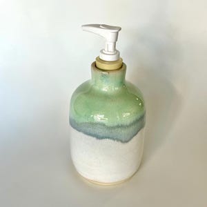 Pu&ograve; includere: Un dispenser di sapone in ceramica con corpo arrotondato e smalto bicolore. La met&agrave; superiore &egrave; di un tenue verde menta che sfuma in una base bianca testurizzata. Un meccanismo a pompa in plastica bianca &egrave; fissato sulla parte superiore.