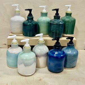 Pu&ograve; includere: Una collezione di dieci dispenser per sapone in ceramica in varie tonalit&agrave; di blu, verde e bianco. Ogni dispenser presenta un corpo arrotondato con una texture liscia o a coste e un meccanismo a pompa in plastica bianca o nera, su due livelli.