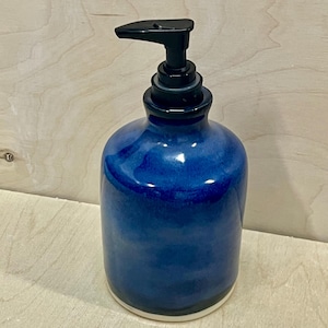 Pu&ograve; includere: Un dispenser di sapone cilindrico in ceramica caratterizzato da una profonda smaltatura blu cobalto lucida con sottili variazioni tonali. Il contenitore ha un corpo liscio e arrotondato ed &egrave; dotato di una pompa in plastica nera.
