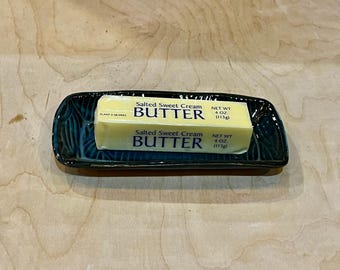 May include: A rectangular, dark teal ceramic butter dish with a glossy, textured finish. Resting inside is a single stick of Salted Sweet Cream BUTTER, clearly labeled with the weight of 4 OZ (113g) printed on its yellow paper wrapper.