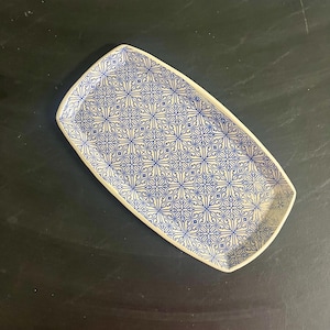 May include: Rectangular ceramic serving platter with a blue and white floral pattern. The platter has a slightly raised edge and rounded corners. The design features a repeating pattern of stylized flowers and swirls.